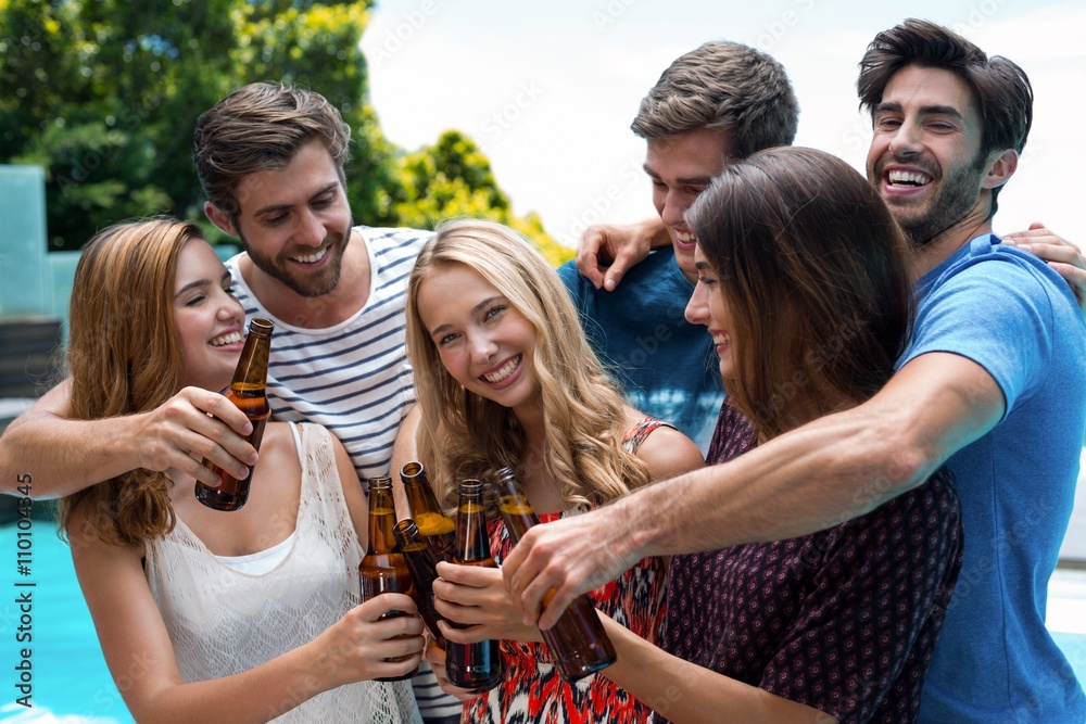 Group of friends toasting beer bottles near pool