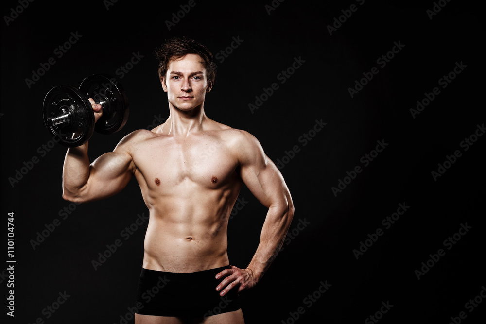 Handsome athletic man with dumbbells confidently looking forward. Strong bodybuilder with six pack, perfect abs, shoulders, biceps, triceps and chest. Great fitness body. Ideal for commercial 