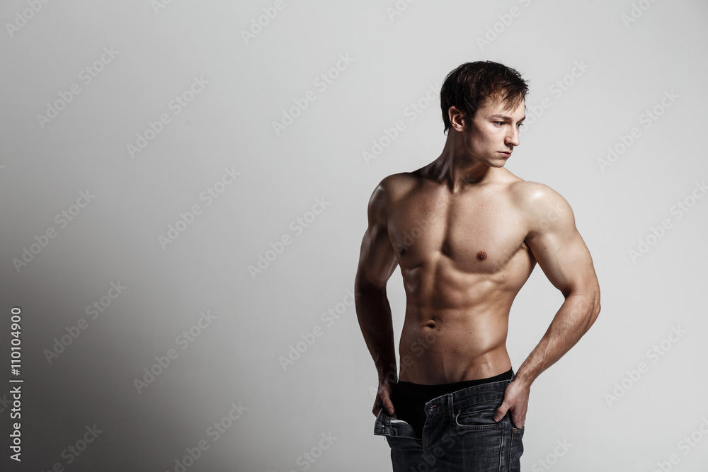Handsome athletic man looking side in unbuttoned jeans. Strong bodybuilder with six pack, perfect abs, shoulders, biceps, triceps and chest. Great fitness body. Ideal for commercial. Gray background Handsome athletic man looking side in unbuttoned jeans. Strong bodybuilder with six pack, perfect abs, shoulders, biceps, triceps and chest. Great fitness body. Ideal for commercial. Gray background