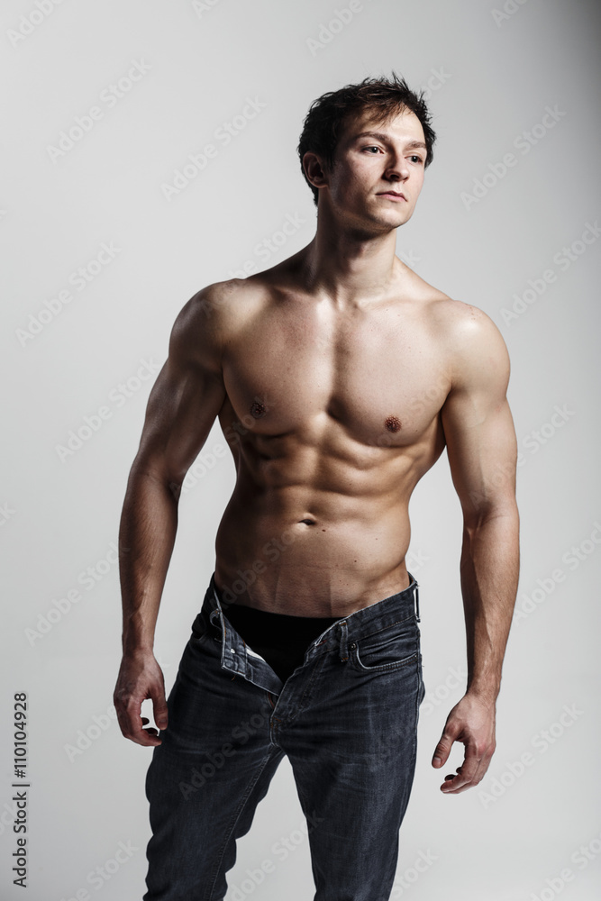 Muscular male model bodybuilder with unbuttoned jeans. Studio shot on gray background. Fitness MODEL. Great for commercial. Ideal fitness body with six pack, perfect abs, shoulders. 