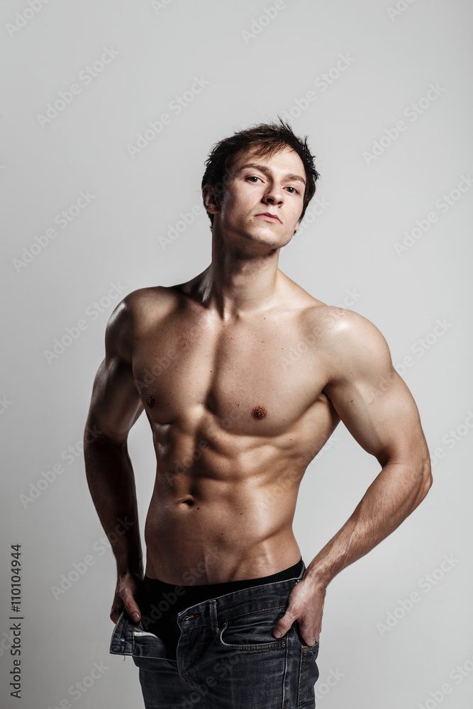 Muscular male model bodybuilder with unbuttoned jeans. Studio shot on gray background. Fitness MODEL. Great for commercial. Ideal fitness body with six pack, perfect abs, shoulders. 