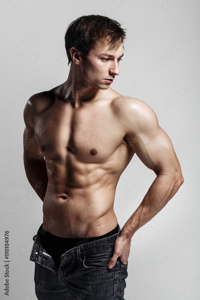 Muscular male model bodybuilder with unbuttoned jeans. Studio shot on gray background. Fitness MODEL. Great for commercial. Ideal fitness body with six pack, perfect abs, shoulders. Muscular male model bodybuilder with unbuttoned jeans. Studio shot on gray background. Fitness MODEL. Great for commercial. Ideal fitness body with six pack, perfect abs, shoulders.