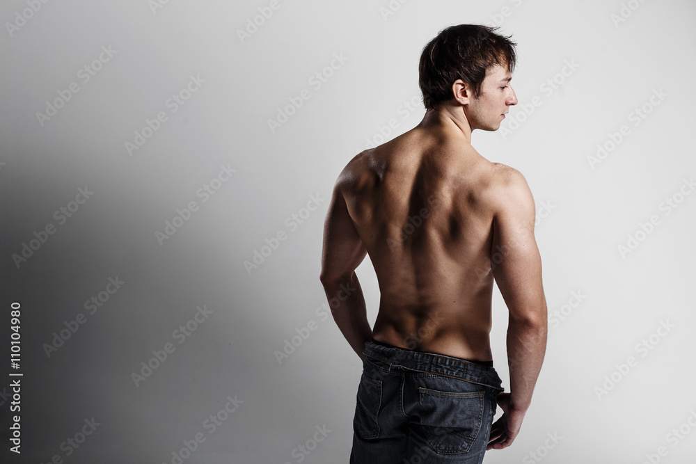 Handsome athletic man looking side in unbuttoned jeans. Strong bodybuilder  with six pack, perfect abs, shoulders, biceps, triceps and chest. Great  fitness body. Ideal for commercial. Gray background Stock Photo