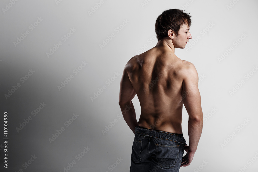 Handsome athletic man looking side in unbuttoned jeans. Strong bodybuilder with six pack, perfect abs, shoulders, biceps, triceps and chest. Great fitness body. Ideal for commercial. Gray background Handsome athletic man looking side in unbuttoned jeans. Strong bodybuilder with six pack, perfect abs, shoulders, biceps, triceps and chest. Great fitness body. Ideal for commercial. Gray background