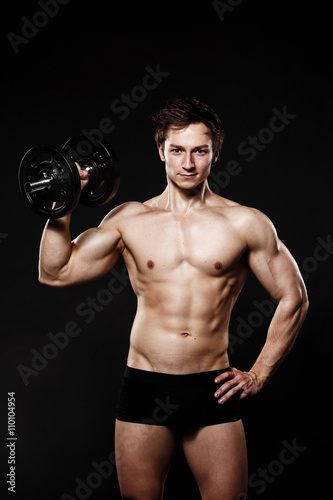 Handsome athletic man with dumbbells confidently looking forward. Strong bodybuilder with six pack  perfect abs  shoulders  biceps  triceps and chest. Great fitness body. Ideal for commercial 