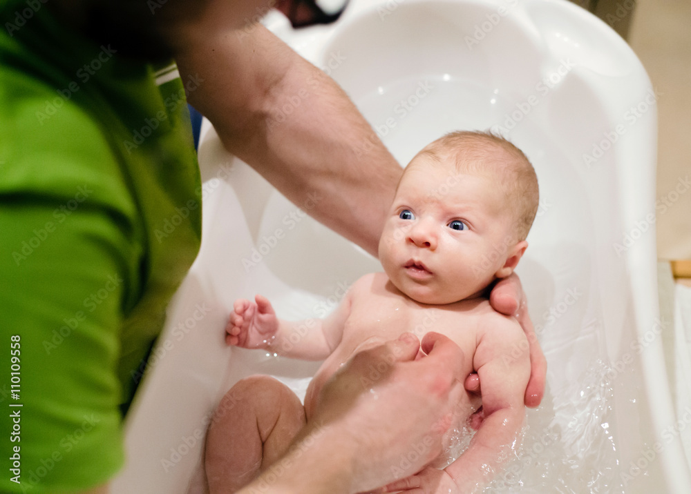 Unrecognizable young father bathing his little baby son Unrecognizable young father bathing his little baby son