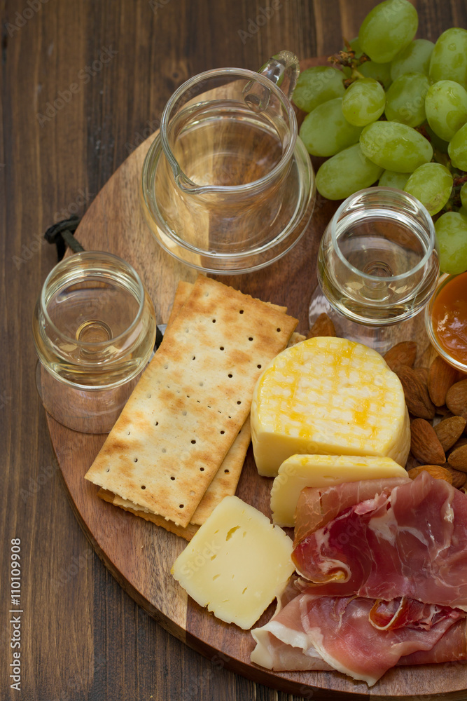 prosciutto with cheese, cookies, grapes and white wine on brown wooden background prosciutto with cheese, cookies, grapes and white wine on brown wooden background