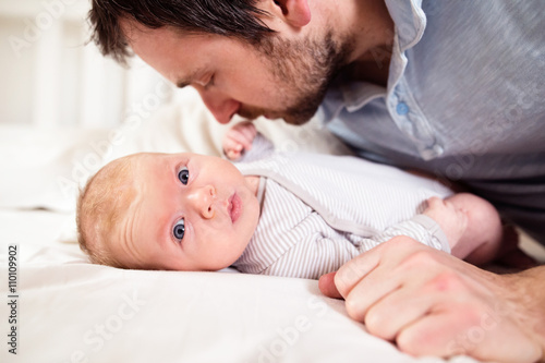 Baby boy lying on bed, held by his father