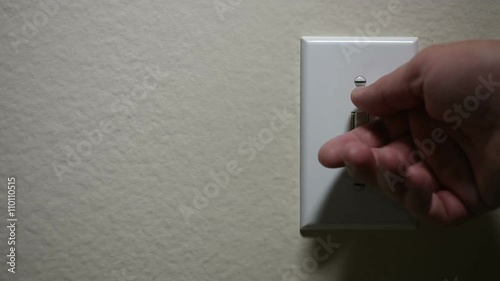 A hand turns off and turns on a light switch photo