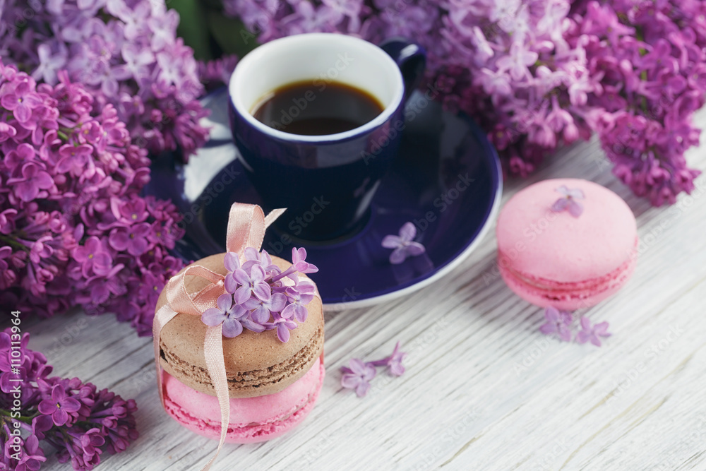 Cup of black coffee, lilac flowers and sweet pastel french macar
