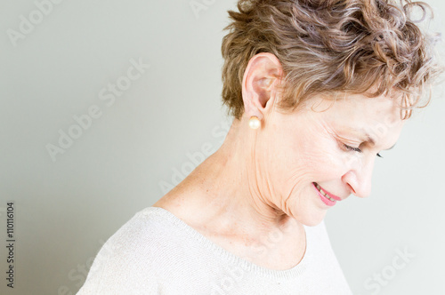 Profile view of older woman in beige top looking down thoughtfully