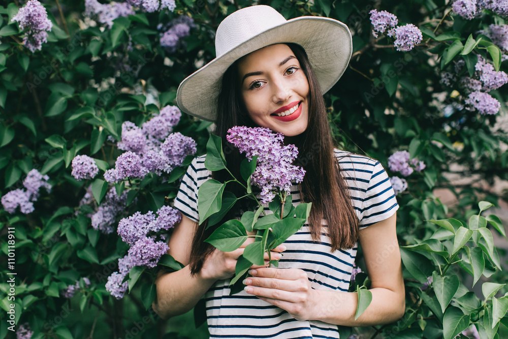 Portrait of stylish girl hipster on the street among a blossoming lilac