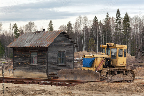 Yellow bulldozer in the sand near the wooden house in a forest