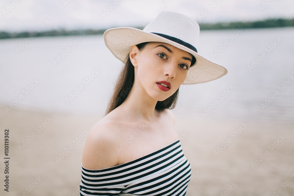 Portrait of a beautiful stylish and fashionable girl in hat near the water