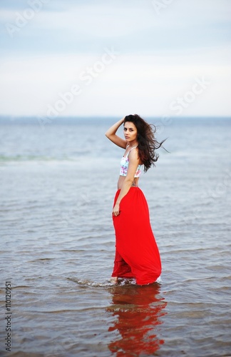 beautiful sexy girl with long hair standing in water and romantically looks at the camera in a red skirt