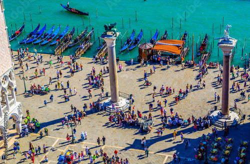 Tourists on San Marco square feed large flock of pigeons in Venice. San Marco square is the largest and most famous square in Venice.