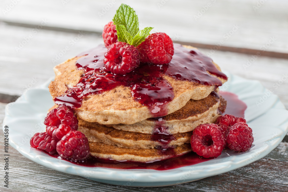 Whole wheat oatmeal pancakes with boysenberry sauce topped with red raspberries and a mint sprig macro shot on a weathered barn wood table Whole wheat oatmeal pancakes with boysenberry sauce topped with red raspberries and a mint sprig macro shot on a weathered barn wood table
