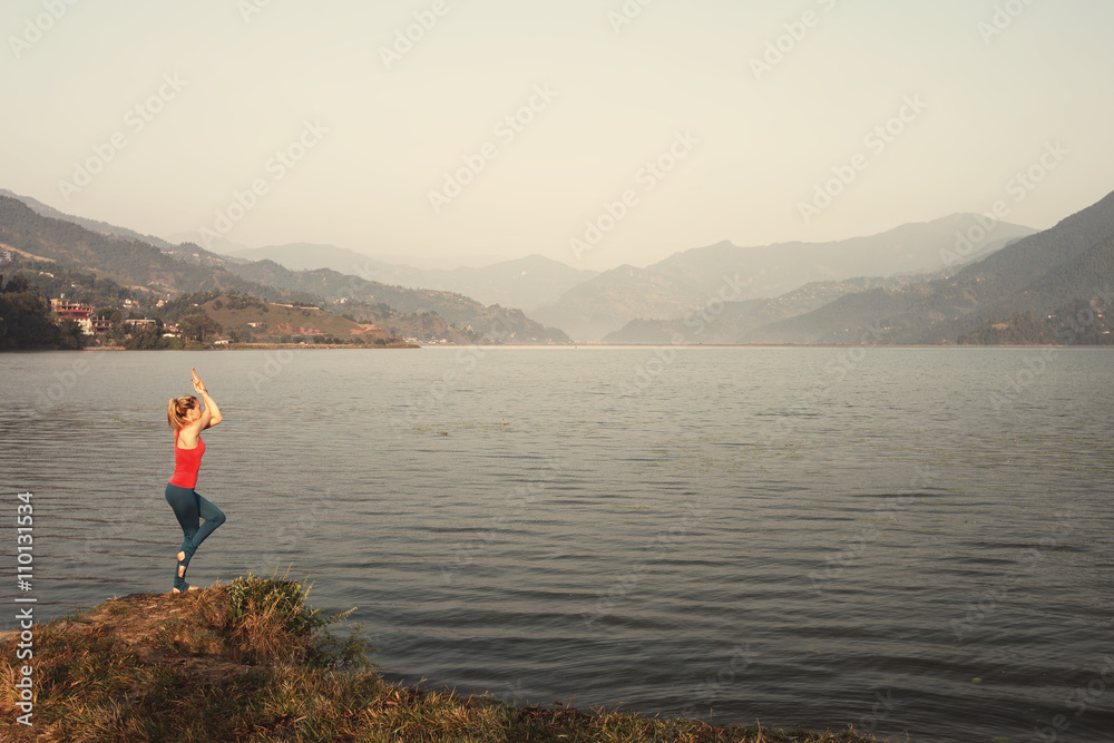 Young girl doing yoga exercise in beautiful mountain lake landscape. Summer, sport outdoor, relaxation