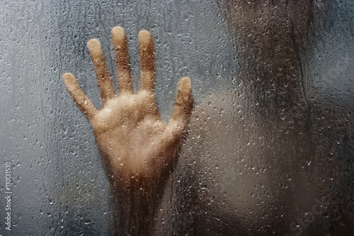 human hand and unrecognizable silhouette behind wet glass in shower