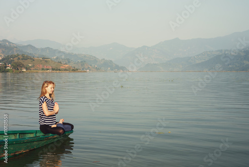 Young Woman in lotus pose relaxing and doing yoga meditation on the boat on mountain lake in morning