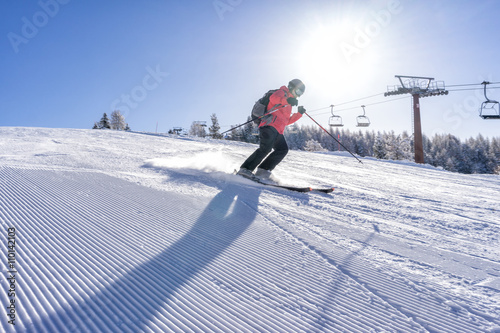 Female skiier dressed in red jacket enjoys slopes in Italy with sun behind her.