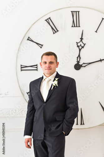 Man in black suit with big clock on background, time concept