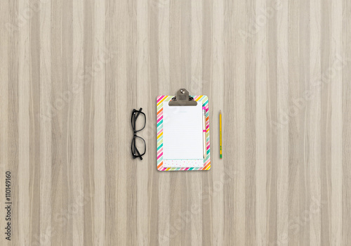 Office desk top view image with notepad, pencil and glasses. Wooden background