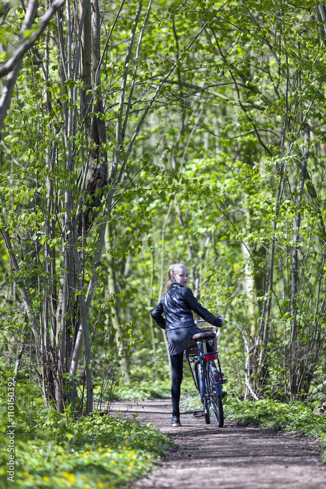 Obraz premium young blond girl with bicycle amongst fresh green spring foliage