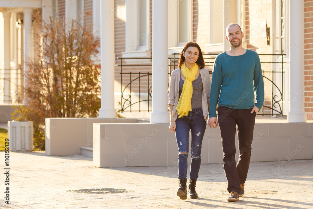 Young couple man and woman walking on the street looking at the camera strong back light