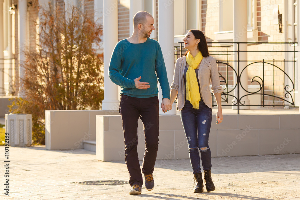 Fototapeta premium Young couple man and woman walking on the street talking to each other strong back light