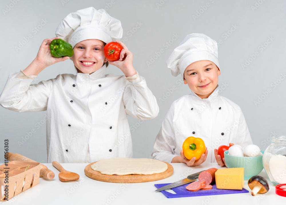 boy and girl in white uniform by the table prepare pizza boy and girl in white uniform by the table prepare pizza