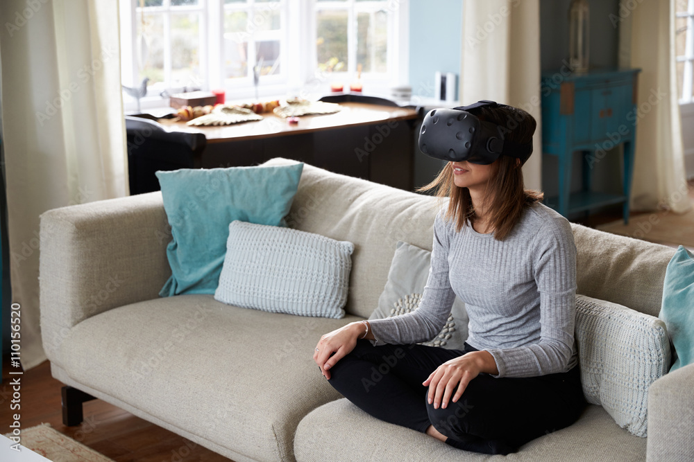 Woman Sits On Sofa At Home Wearing Virtual Reality Headset Woman Sits On Sofa At Home Wearing Virtual Reality Headset