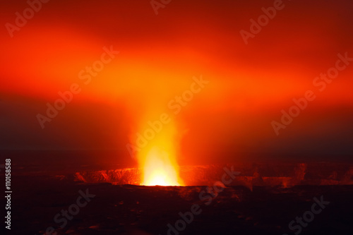 View of a glowing lava lake at Volcanoes National Park on the Big Island of Hawaii. The vibrant orange and red colors of the molten lava create a striking visual against the dark, smoky ba