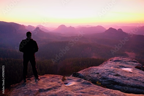 Tall man in black on cliff and watch to mountain sunrise.Silhouette in selfconfident pose