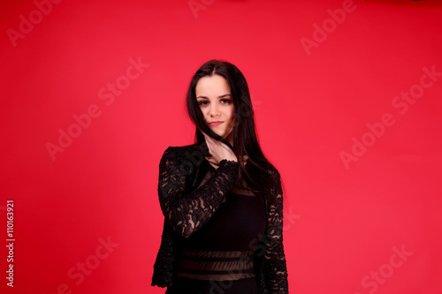 Young girl in a classic black dress and black shoes on red background