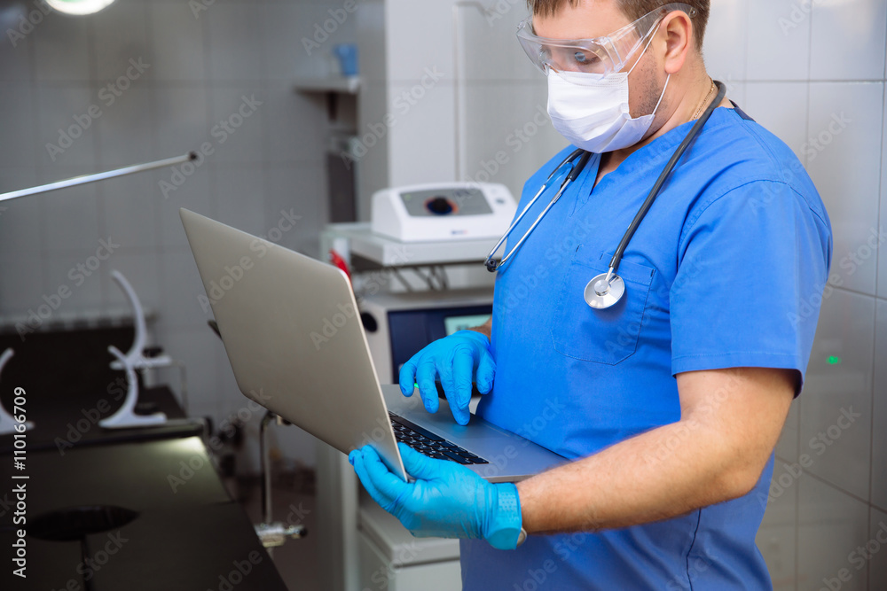Naklejka premium adult doctor in mask with laptop and medical tools in operating room at the hospital
