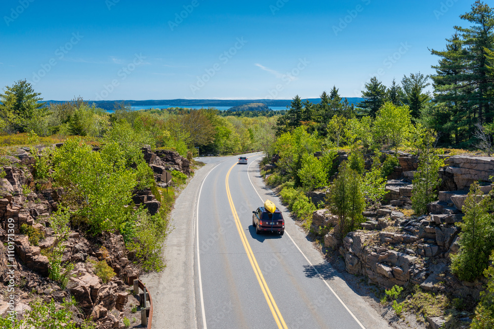 Cars driving on road in Acadia National Park, Maine, USA. The last car holds a canoe on its roof.