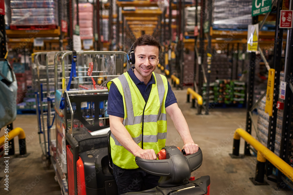 Obraz premium Man on tow tractor at distribution warehouse looks to camera