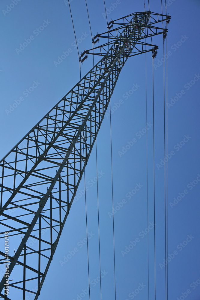 Very high electricity pylon during the sunny day with bright sun and blue sky Very high electricity pylon during the sunny day with bright sun and blue sky