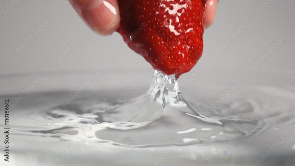 Man's hand drop out fresh tastyred strawberry with green top into water breaking liquid surface with little splash. White background isolated. Super slow motion camera horizontal shot