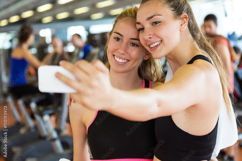 Two sporty young woman using mobile phone in gym.