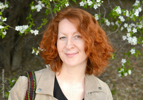 Portrait of a beautiful woman with red curly hair, on a background of a blossoming tree