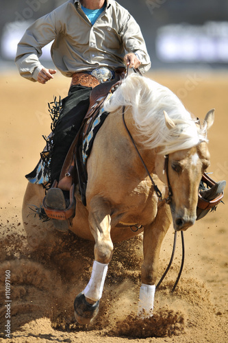 A close up view of a rider sliding the horse in the dirt