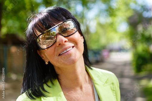 Close-up portrait of cute woman with white smile and sun glasses in outdoor. Happy Lady Dressed in a green jacket and have spring-summer mood