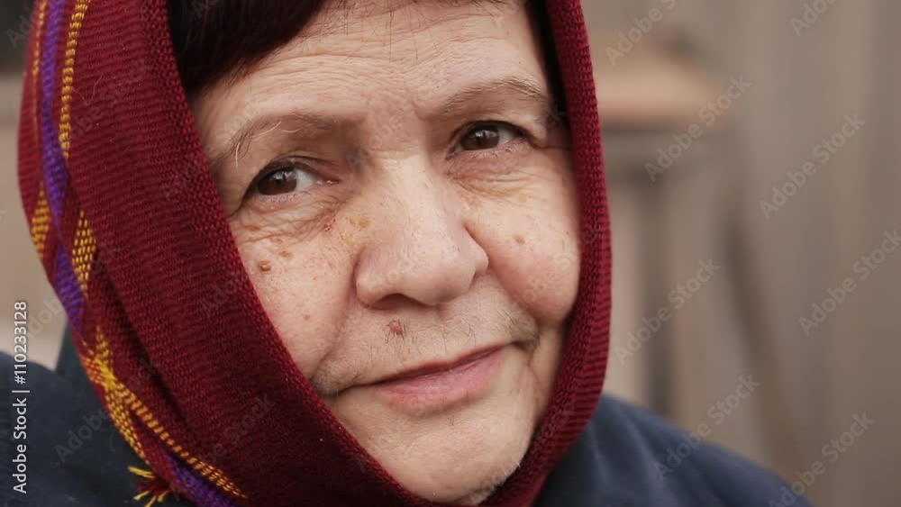 an elderly woman in a scarf smiles sadly outdoors an elderly woman in a scarf smiles sadly outdoors