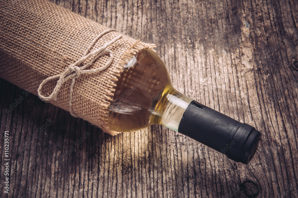 Bottle of white wine in linen on rustic wooden background