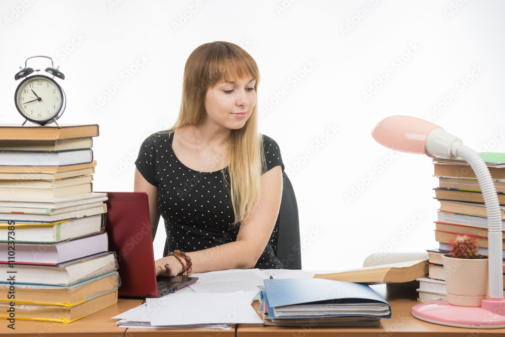 college student smiling with a laptop in gaining information while sitting at a table littered with books in the library