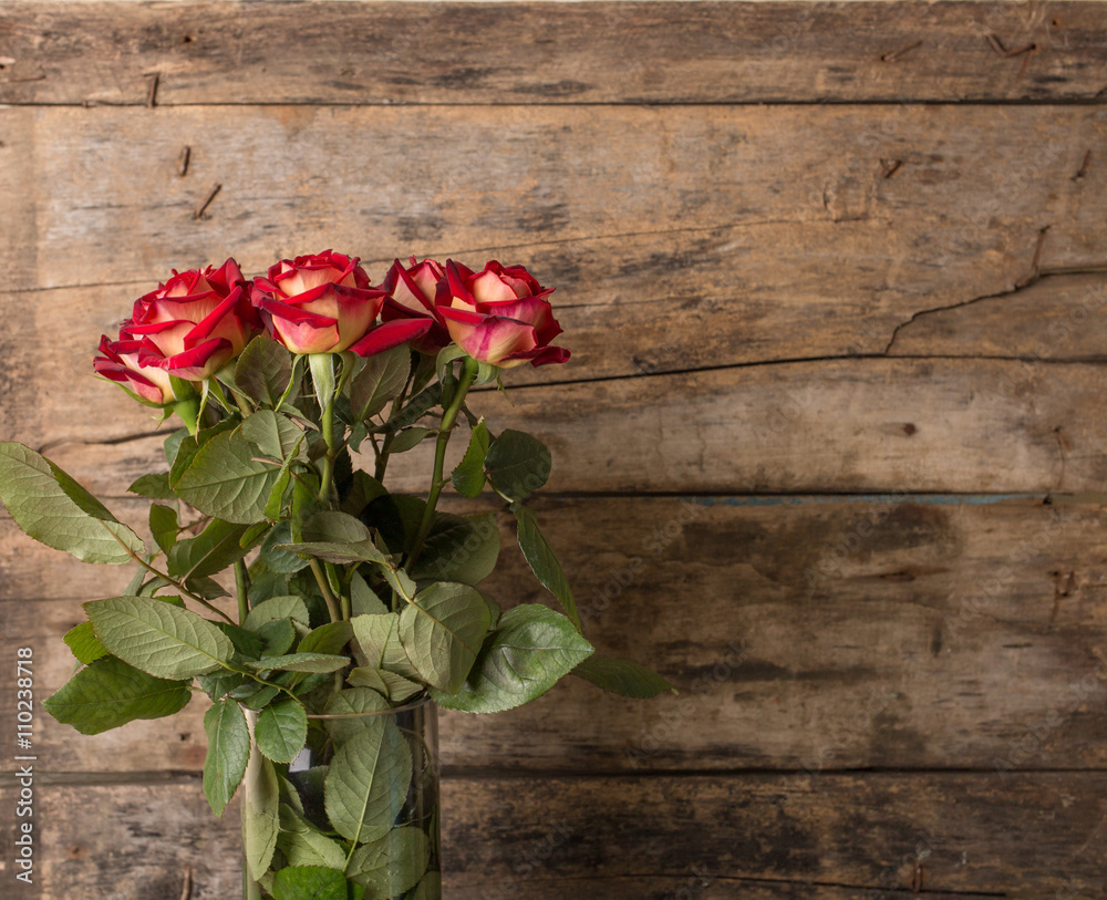 Bunch of red roses in vase on wooden background