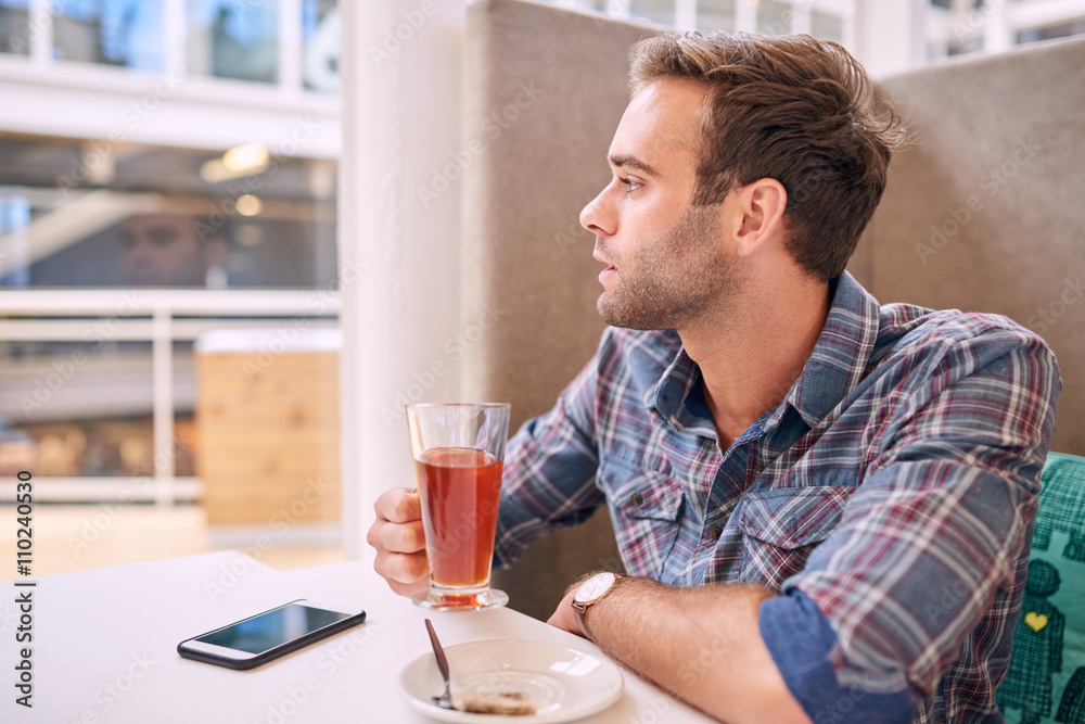 Handsome man looking sideways while holding his tea in cafe Handsome man looking sideways while holding his tea in cafe