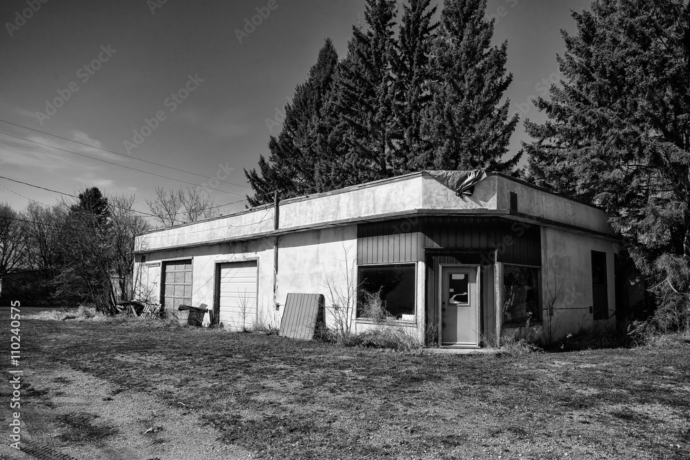 An abandoned stucco garage with two bay doors and junk laying around in black and white An abandoned stucco garage with two bay doors and junk laying around in black and white